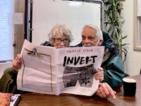 an older couple sitting at a table reading a magazine